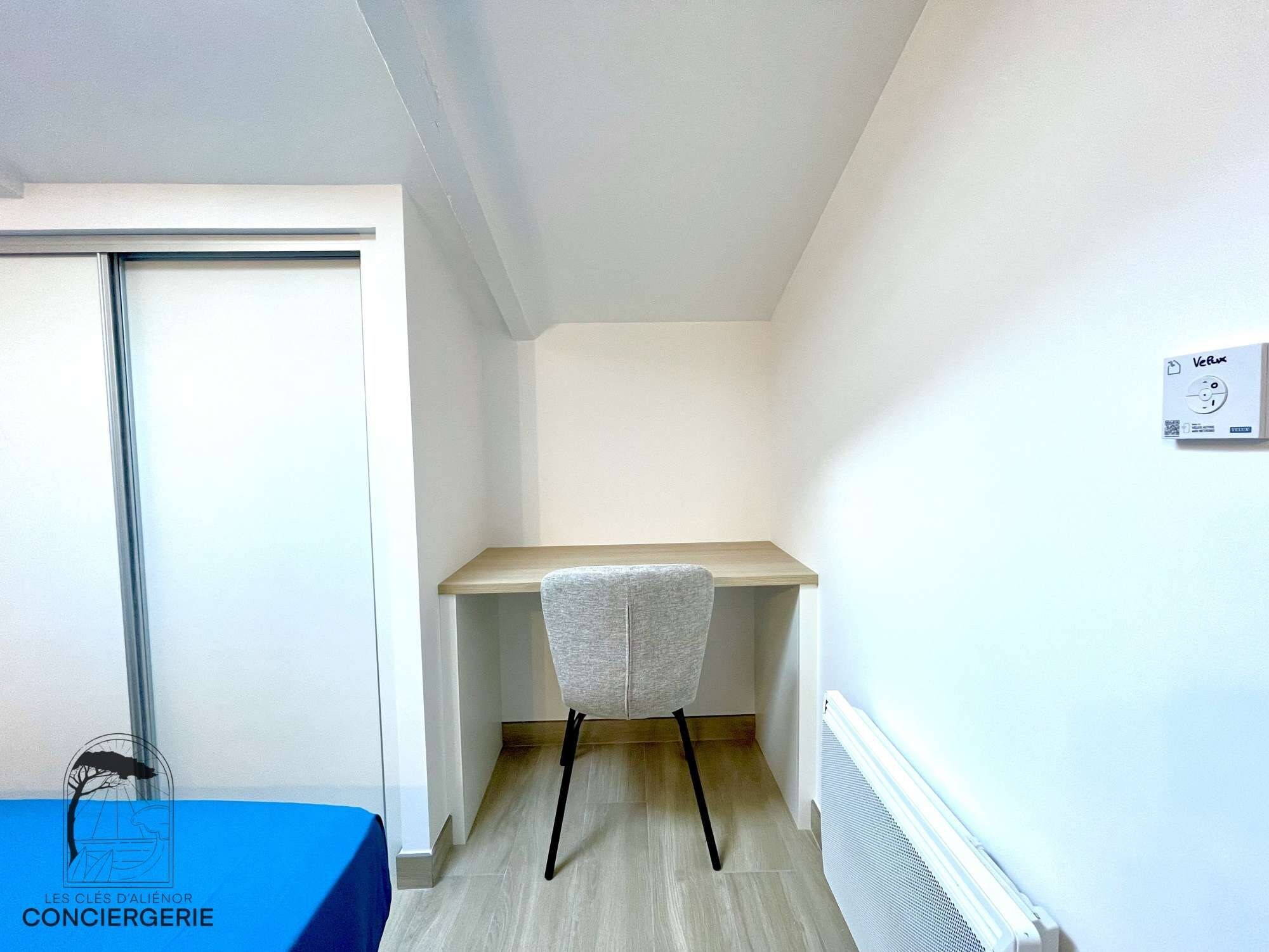 Een kleine, smalle kamer met een bureau, een stoel, een radiator en een deur.