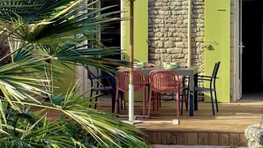 Une terrasse avec une table et des chaises, un parasol jaune et un mur en pierre.
