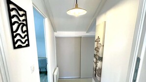 Un couloir avec un luminaire au plafond, un élément décoratif mural et une porte donnant sur une autre pièce.
