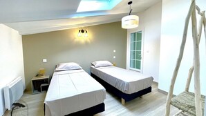 Une chambre avec deux lits simples, une lucarne, un luminaire suspendu et une fenêtre.
