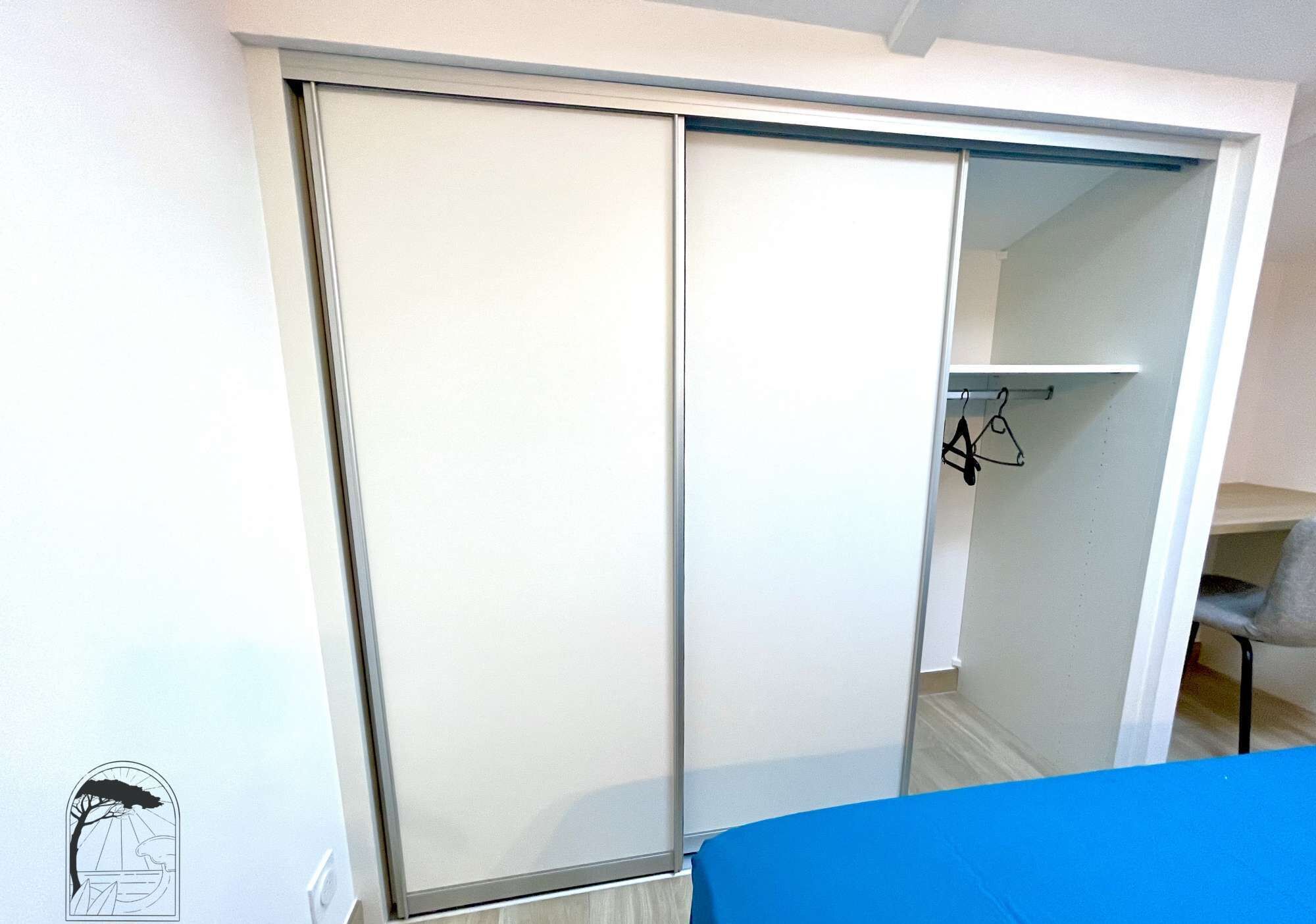 A room with a sliding closet door, a chair, and a small shelf with hanging items.