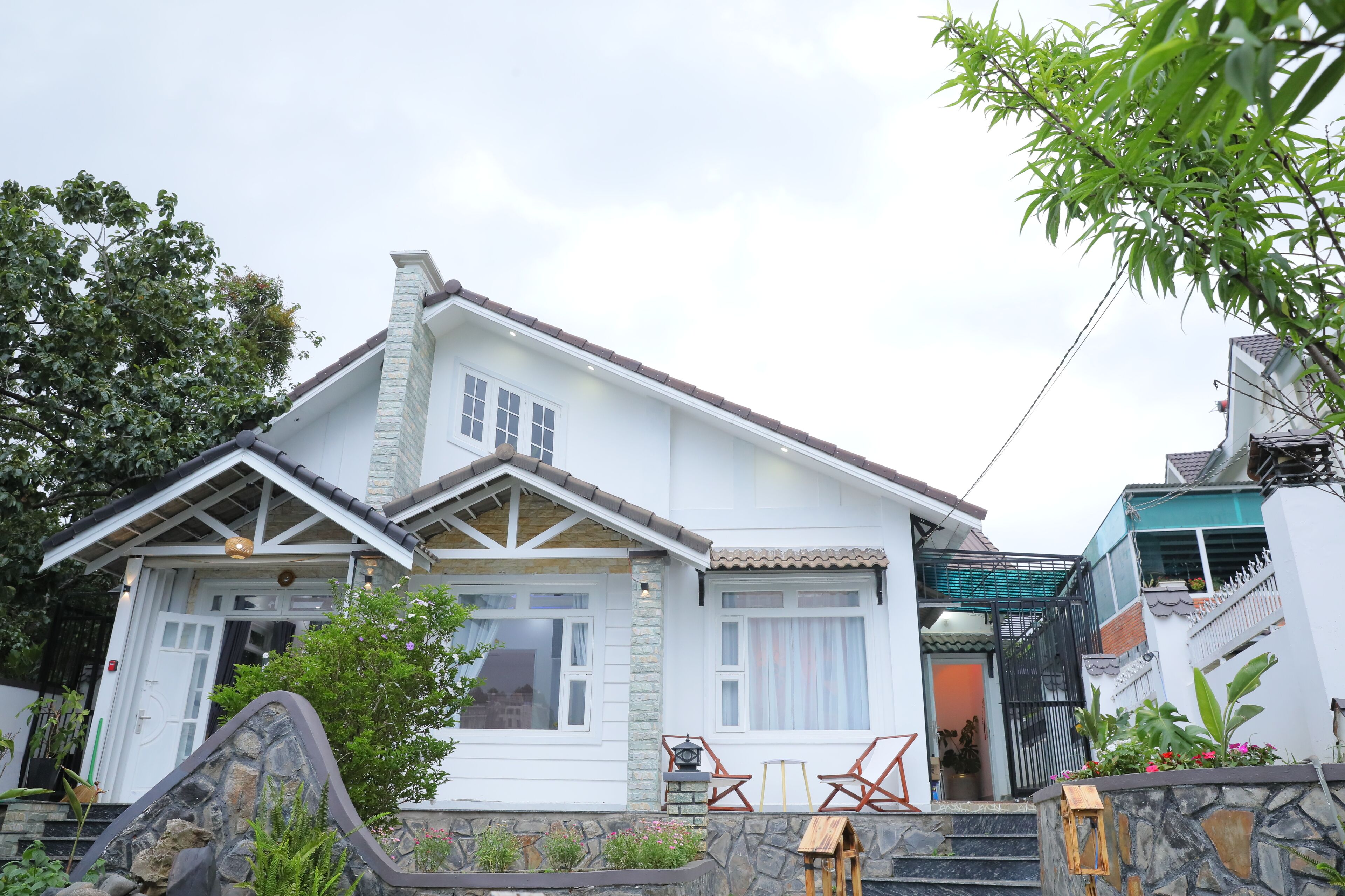 A two-story house with a stone facade, a tiled roof, and a front porch with a wooden bench.