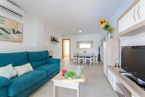 A modern living room with a teal sofa, a coffee table with decorative items, a flat-screen TV, and a dining area in the background. - Apartment 'Calma Mar' with Shared Pool, Wi-Fi and Air Conditioning (Los Mártires)
