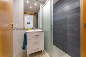 A bathroom with a white vanity, a mirror, a towel rack, and a shower area with a dark tiled wall.