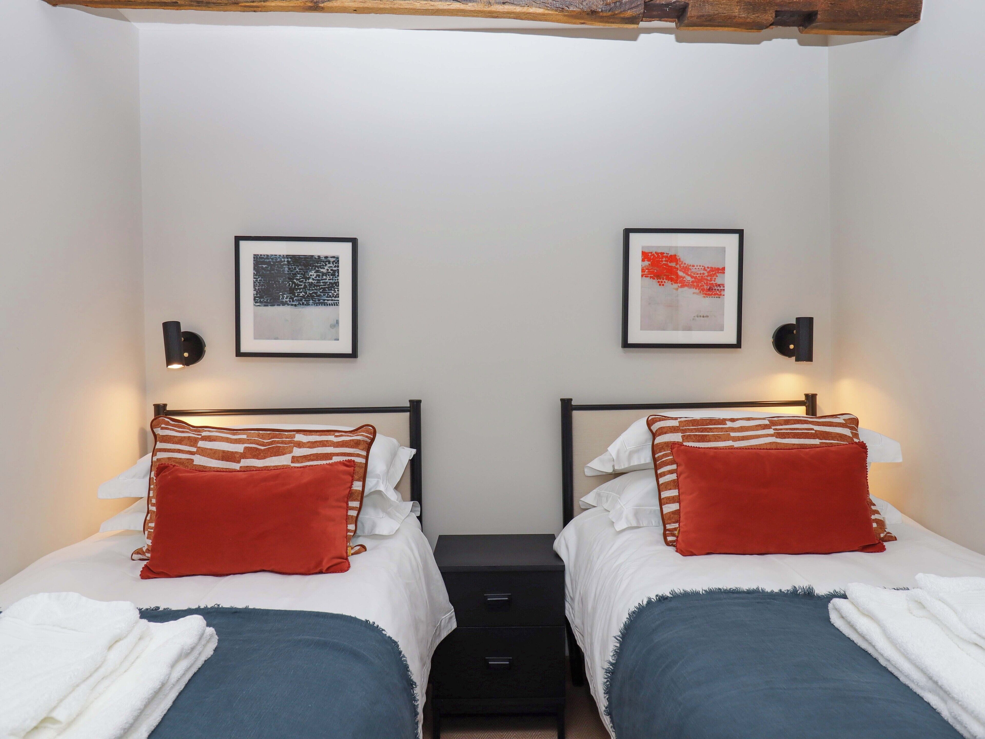 Habitación doble con dos camas, cada una con una almohada roja y una manta azul. Hay obras de arte enmarcadas en la pared sobre cada cama.