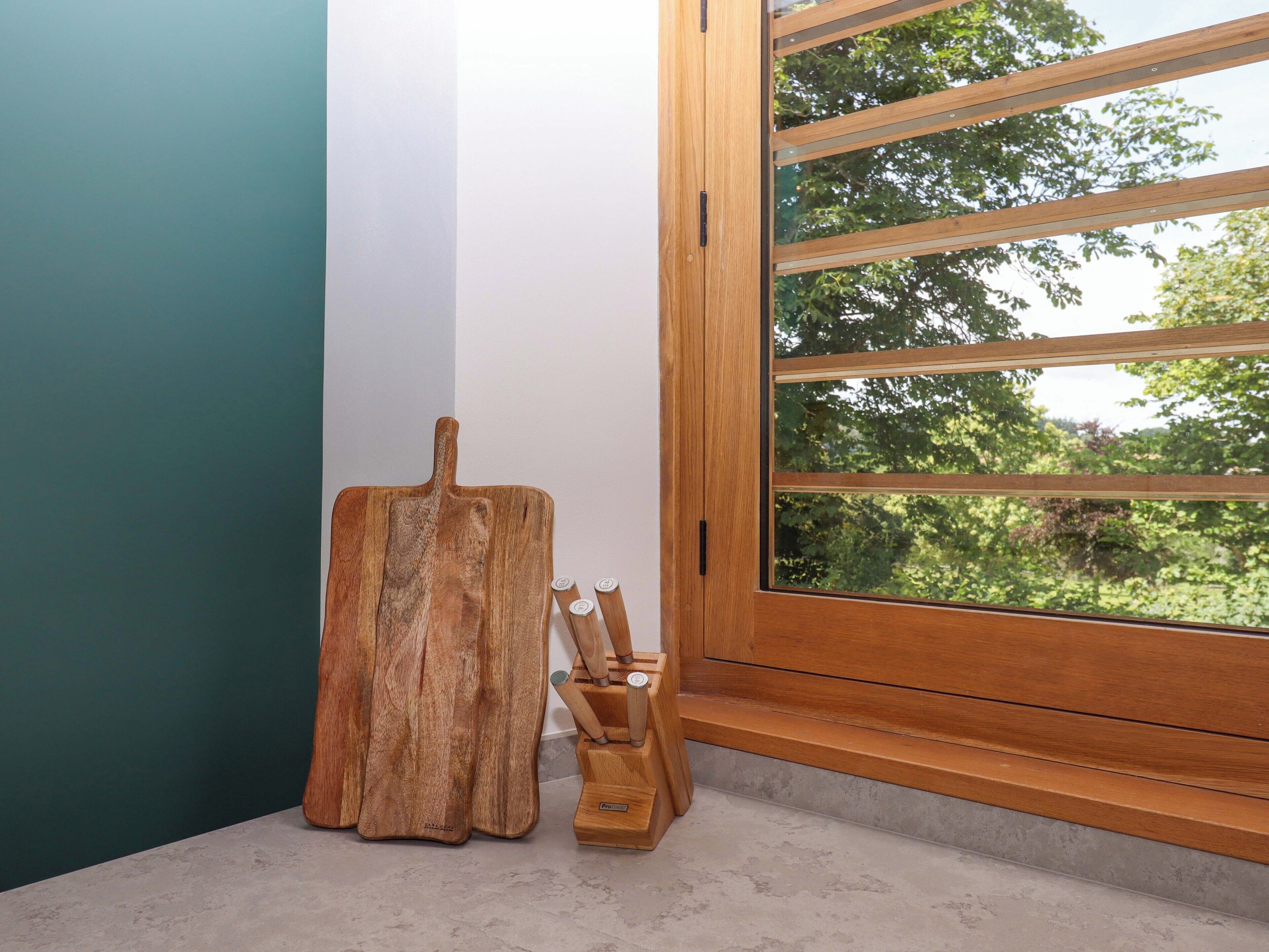 A corner of a room with a wooden cutting board and a knife block by a window with a view of trees.