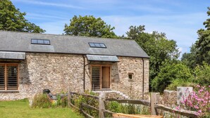 A stone building with a wooden door and windows, a hot tub in the foreground, and a wooden fence. - Lower Walreddon Barn (Tavistock)