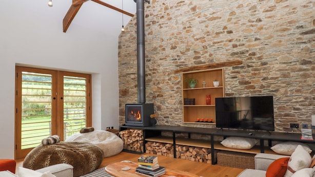 A cozy living room with a stone wall, a fireplace, a TV, and comfortable seating. - Lower Walreddon Barn (Tavistock)