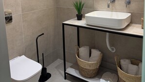 A modern bathroom with a toilet, sink, and mirror. There are baskets on the floor and a plant on the sink.