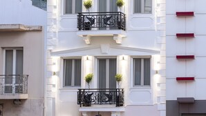 A two-story building with a white facade, balconies with black railings, and green awnings over the entrance doors.