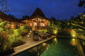 Un espace aménagé au bord de la piscine, avec des chaises longues, une terrasse en bois et un bâtiment doté d’un toit recouvert de tuiles.