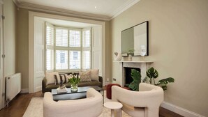 A living room with a sofa, armchairs, a coffee table, a fireplace, and a large window. - Redbrick on Langton (London)