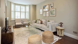 A living room with a sofa, chairs, a coffee table, and a large window with blinds. - Redbrick on Langton (London)