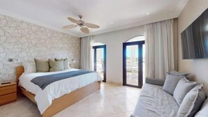 Une chambre à coucher avec un lit, une table de chevet, un canapé, un ventilateur de plafond et un téléviseur fixé au mur.