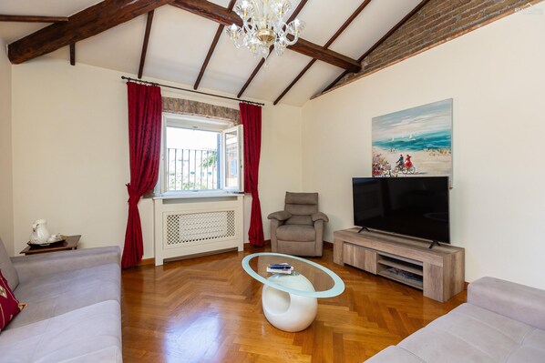 Un soggiorno con soffitto in legno, una grande televisione, un divano, una poltrona e un tavolino in vetro.