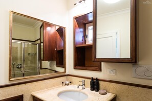 Un bagno con lavabo in marmo, armadietti in legno e un grande specchio che riflette l'area doccia.