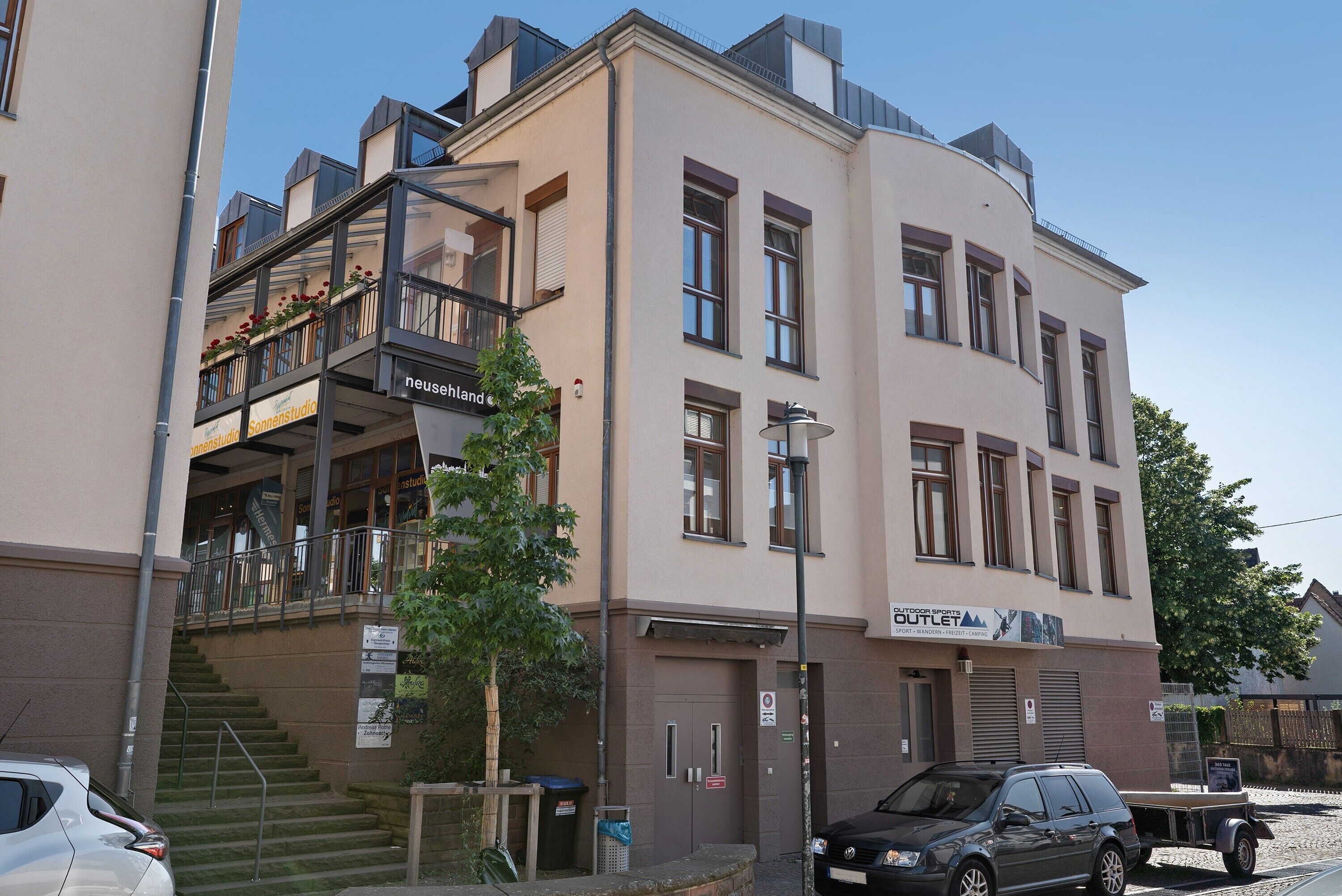 En bygning med flere etager, en balkon og en trappe, der fører op til en overetage. Skilt med 'Outdoor Sports Outlet'.