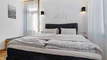 En pænt redt seng med gavl, et natbord, en vægmonteret lampe og et skilt med teksten 'time to RELAX'.