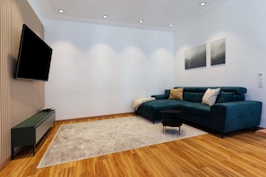 Un salon moderne avec un téléviseur à écran plat, un canapé vert, une petite table d’appoint et un plancher en bois.