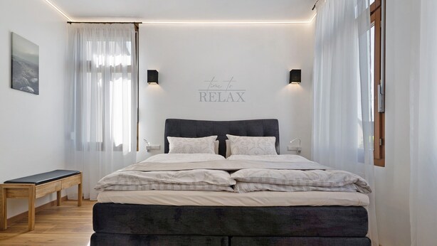 Une chambre à coucher comprenant un lit, des tables de chevet, un banc et un panneau fixé au mur.