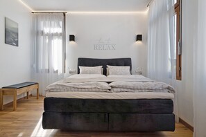 Une chambre à coucher comprenant un lit, des tables de chevet, un banc et un panneau fixé au mur.