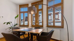 Un espace repas avec une table et des chaises en bois, de grandes fenêtres et un lampadaire.