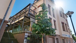 Un immeuble à plusieurs étages doté d’un balcon, d’un espace extérieur aménagé pour s’asseoir et d’une enseigne indiquant « Neusehland ».
