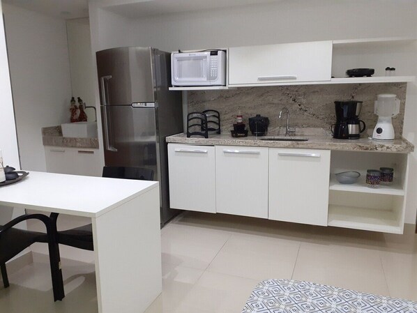 Cocina compacta equipada con refrigerador, microondas, cafetera y un pequeño comedor con mesa y sillas.