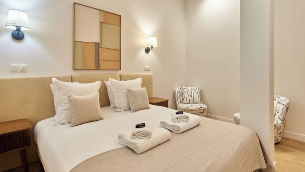 A hotel room with a bed, two wall-mounted lamps, a mirror, a chair, and a bedside table. - Elegant Apartment With Buttes-chaumont Park (Paris)