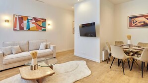 A modern living room with a sofa, coffee table, and dining area with chairs and a TV mounted on the wall. - Elegant Apartment With Buttes-chaumont Park (Paris)