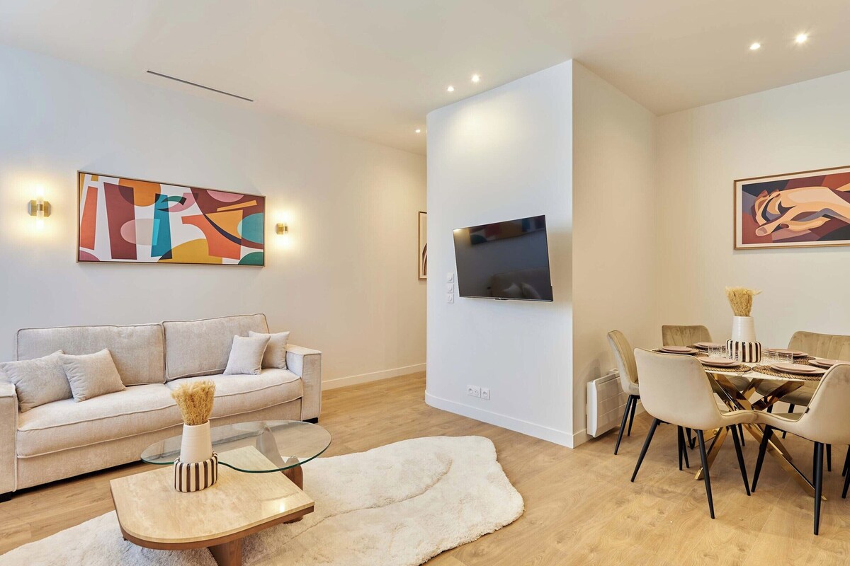A modern living room with a sofa, coffee table, and dining area with chairs and a TV mounted on the wall.