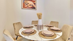 A round dining table with beige upholstered chairs, a white vase with dried plants, and a framed abstract painting on the wall. - Elegant Apartment With Buttes-chaumont Park (Paris)