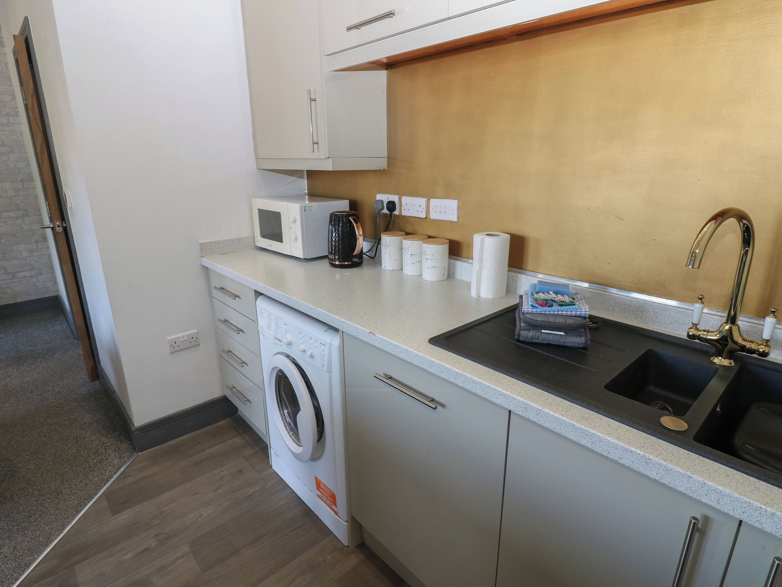 A compact kitchen with a washing machine, microwave, and sink.