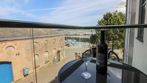 A balcony with a glass table, a wine bottle, and a wine glass. In the background, there is a view of a marina with boats and a brick building. - Quayside Apartments (Whitehaven)