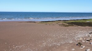 A beach with a clear sky, calm sea, and rocky shoreline. - Quayside Apartments (Whitehaven)