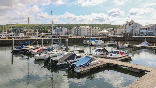 A marina with various boats docked, a wooden pier, and buildings in the background. - Harbourside Apartments (Whitehaven)
