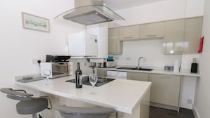 A modern kitchen with a central island, bar stools, a wine bottle, and a toaster. - Harbourside Apartments (Whitehaven)