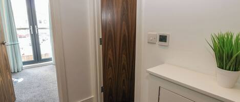 A hallway with a wooden door, a thermostat, and a potted plant.