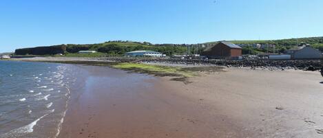 A beach with a rocky shoreline, a building with a sloped roof, and a clear blue sky.