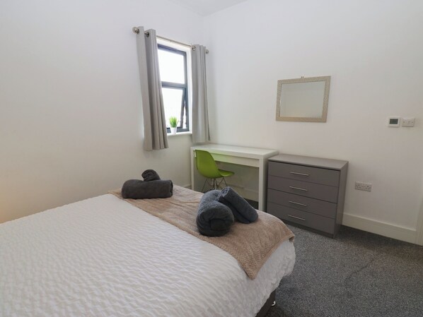 A bedroom with a bed, a desk, a chair, a dresser, and a window with curtains. - Harbour View (Whitehaven)