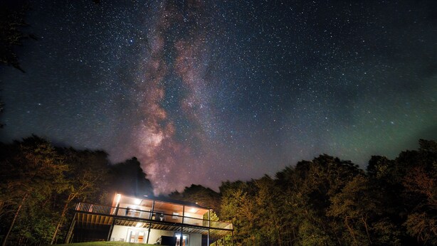 A building with a covered outdoor area, surrounded by trees, under a starry night sky.