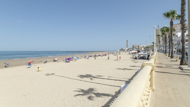 A beach with a paved walkway, palm trees, and umbrellas. - Apartment 'Playa Regla' with Balcony, Wi-Fi and Air Conditioning (Chipiona)