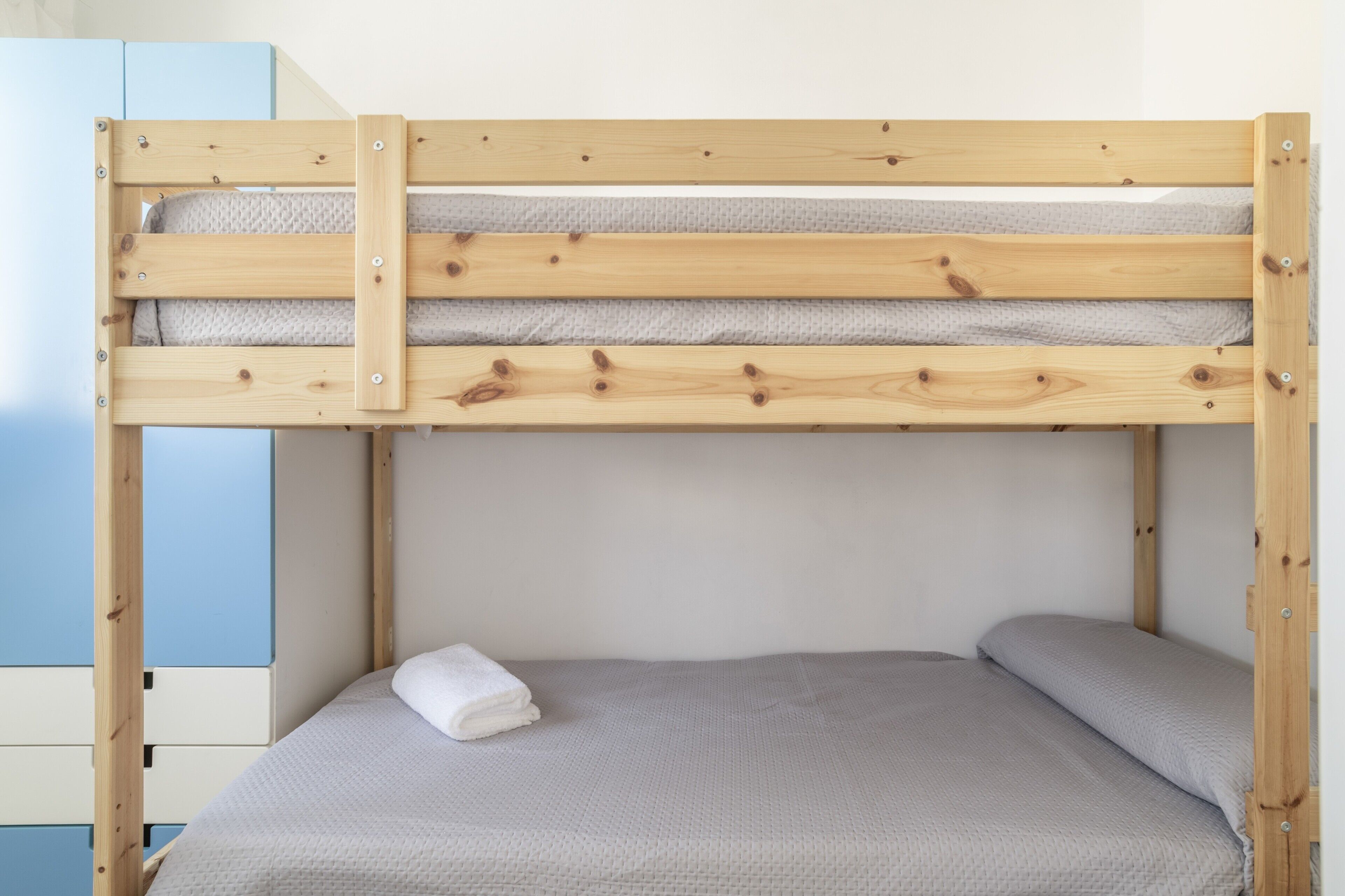 A bunk bed with a grey mattress and a white blanket.
