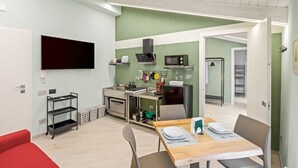 Een moderne keuken met een magnetron, oven en gasfornuis, een eethoek met een tafel gedekt voor twee personen, en een rode bank.