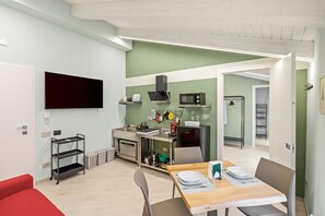 Una cocina moderna con microondas, horno y cocina a gas, un comedor con una mesa para dos, y un sofá rojo.