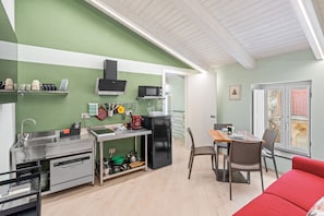 A compact kitchen with a sink, microwave, and refrigerator, a dining area with a table and chairs, and a red sofa.