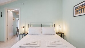 Een net opgemaakt bed met twee kussens, twee nachtkastjes met lampen, en een lijst met een foto aan de muur.