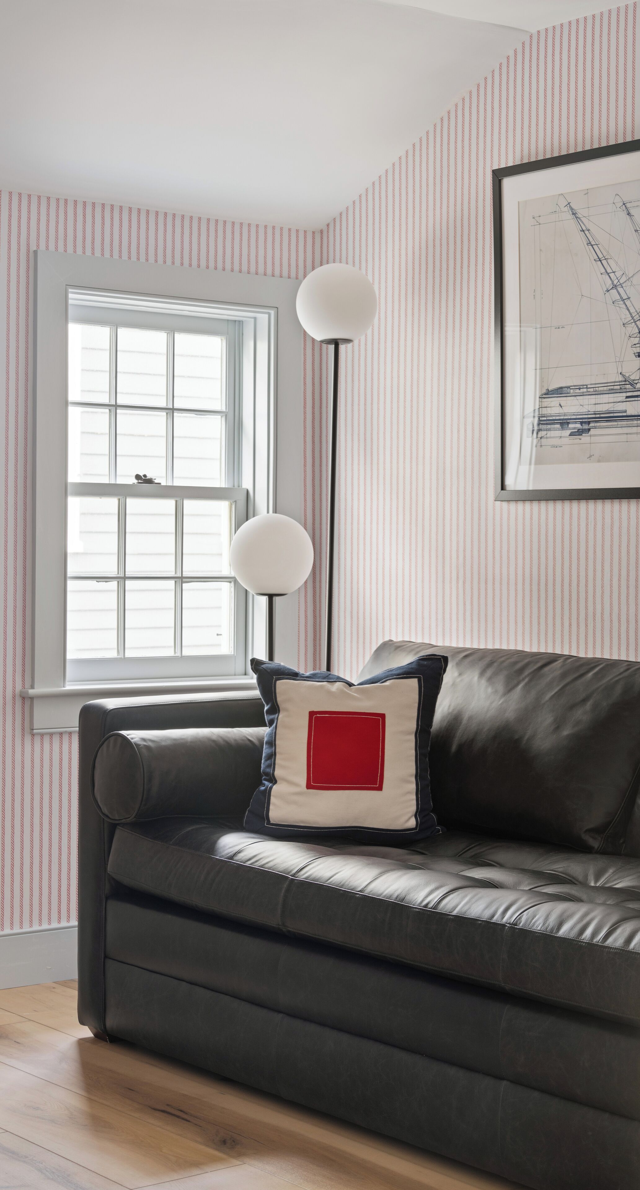 A room with a dark leather sofa, a window with blinds, a floor lamp, and a striped wallpaper pattern.