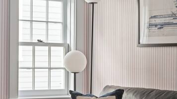 A room with a dark leather sofa, a window with blinds, a floor lamp, and a striped wallpaper pattern.