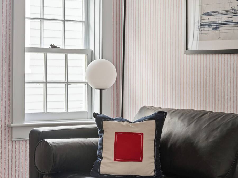 A room with a dark leather sofa, a window with blinds, a floor lamp, and a striped wallpaper pattern.